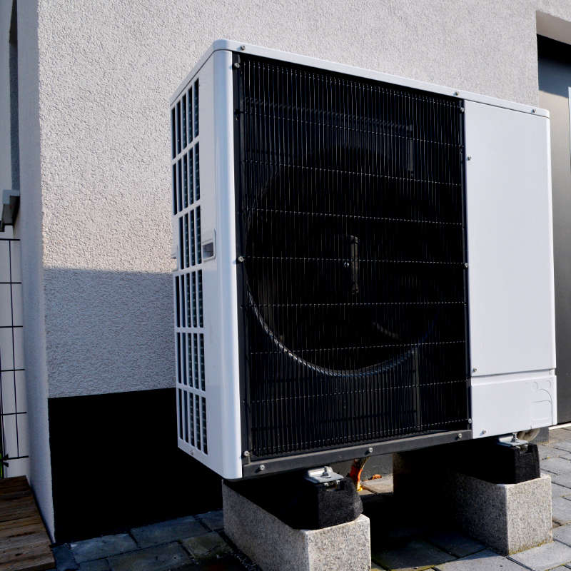 Das Bild zeigt das Klimagerät einer Wärmepumpe vor einem Einfamilienhaus.