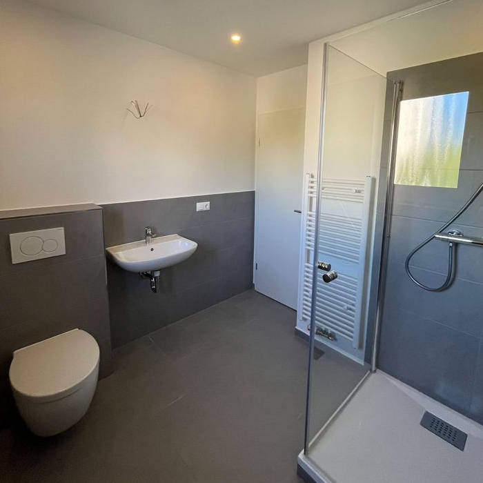 Das kernsanierte Badezimmer samt neuer Fliesen, neuer Decke mit LED-Spots, WC, Waschbecken und Dusche mit Eckeinstieg aus Glas, 90x90 cm.