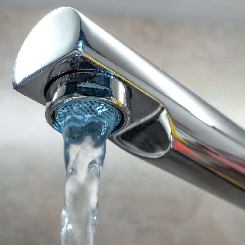 Das Bild zeigt einen verchromten Wasserhahn in Nahaufnahme aus welchem gerade frisches Leitungswasser fließt.