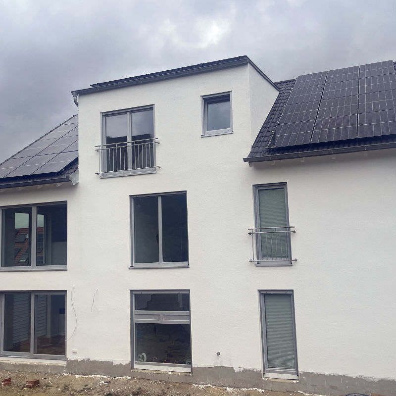 Das Bild zeigt ein neu gebautes, nahezu vollständig fertiggestelltes Einfamilienhaus mit Solaranlage auf dem Dach.